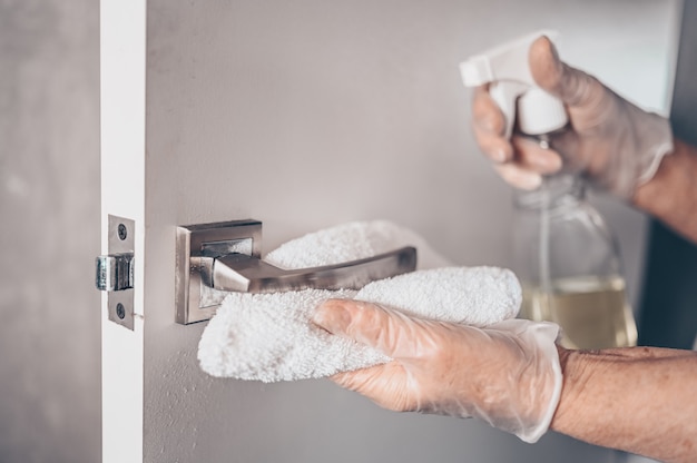 Prévention femme de ménage essuyant la poignée de porte avec un spray désinfectant antibactérien pour tuer le virus sur les surfaces en contact ou toucher la poignée de la salle de bain publique avec du tissu.