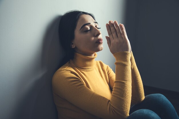 Prier femme assise dans le sol sur une pièce sombre