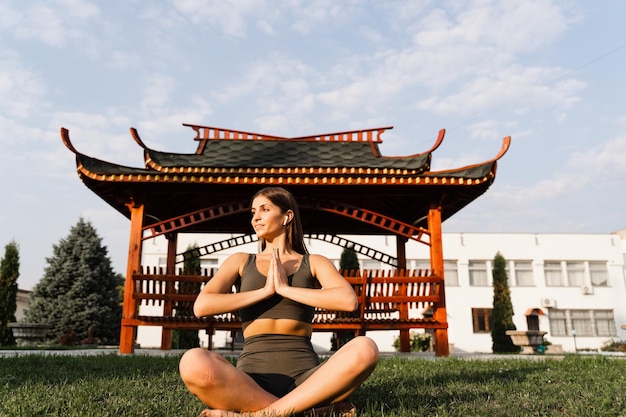 Prier et méditer en position du lotus Une fille en forme est assise et médite à l'extérieur près d'un belvédère chinois