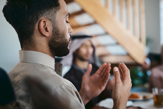 Photo la prière musulmane et la religion tout en étant assis avec la famille et dire une dua ou une prière avant de rompre le jeûne pendant le mois sacré du ramadan homme religieux levant les mains pour prier pendant le repas de l'aïd ou de l'iftar