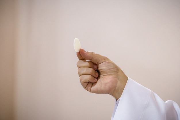 Priest's hand holding wafer, petit pain consacré par le prêtre ordonné, tradition chrétienne et catholique