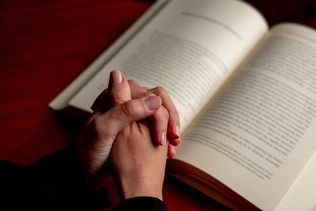 Priez Dieu main féminine en prière sur une table en bois de la Sainte Bible vue rapprochée