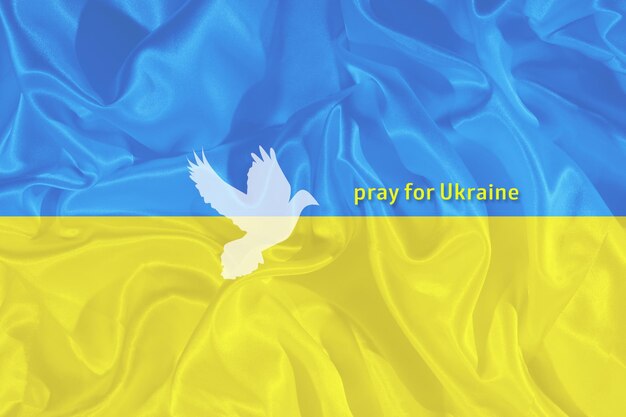 Priez pour le texte de l'Ukraine sur le drapeau ukrainien bleu et jaune avec la silhouette de la colombe de la paix