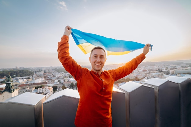 Priez pour l'UkrainexUn homme se tient debout avec le drapeau national ukrainien et l'agite en priant pour la paix au coucher du soleil à LvivxAA symbole de l'indépendance et de la force du peuple ukrainien