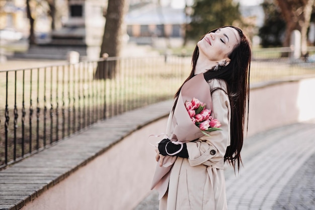 Photo le printemps, l'amour-propre, les soins personnels, le portrait sincère d'une femme heureuse avec un bouquet de tulipes à l'extérieur, une belle femme marchant avec un bouchet de tulipes dans les rues de la ville.