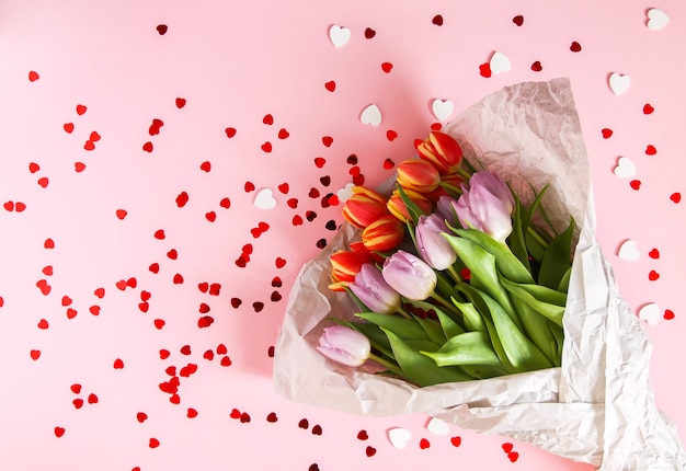 Printemps de belles fleurs de tulipes sur fond rose pastel doux avec des guirlandes de coeur rouge. Fête des mères, carte de voeux composition florale décorative festive.