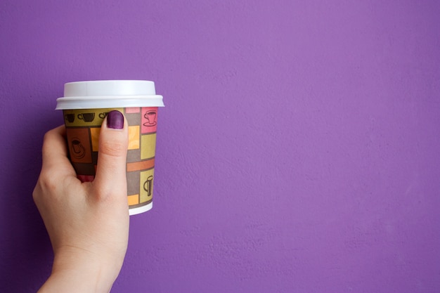 Prise de main de femme prend un café devant le mur violet