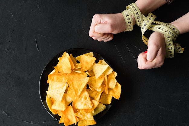 La prise de poids malsaine de collations de restauration rapide due à de mauvaises habitudes alimentaires femme mains liées avec un ruban à mesurer plaque de chips est interdite