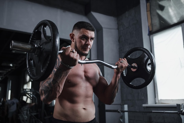 Prise de vue en angle bas d'un bel athlète masculin tatoué déchiré travaillant avec des haltères à la concentration