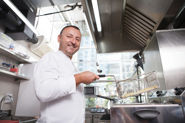 Prise de vue en contre-plongée d'un chef masculin joyeux souriant à la caméra, tout en préparant des frites