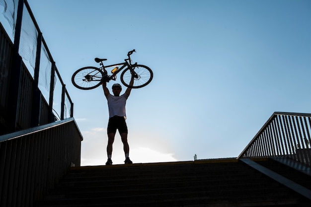 Prise de vue en contre-plongée d'un cycliste masculin en bonne santé tenant victorieusement son vélo au-dessus de sa tête, espace de copie