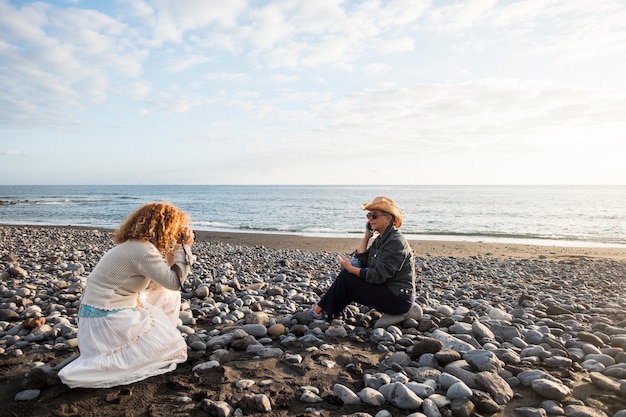 Prise de vue avec deux femelles. un photographe et une femme mûre parlant au téléphone pour représenter un style de vie agréable sur la plage. travail de concept de stock et de publicité