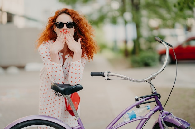 Photo prise de vue en extérieur d'une superbe femme aux cheveux rouges couvre la bouche avec les deux paumes