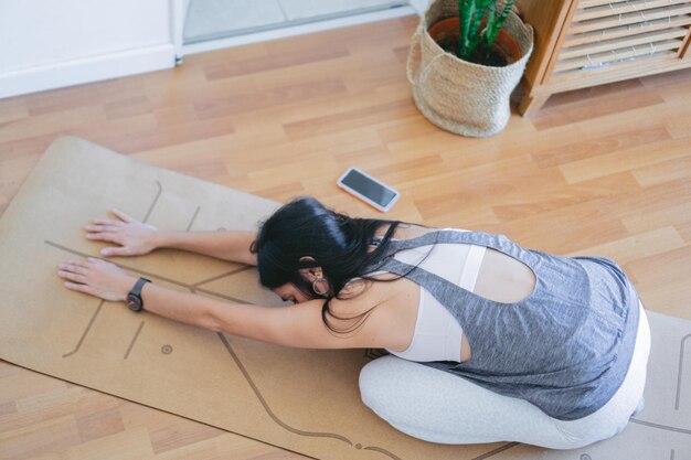 Prise de vue en grand angle d'une jeune femme méconnaissable faisant la pose de yoga balasana sur un tapis dans son salon