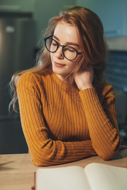 Prise de vue en intérieur d'une femme au gingembre rêveuse travaillant sur le temps libre de la critique de livres avec le concept de passe-temps littéraire