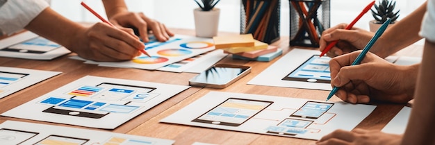 Prise de vue panoramique de l'équipe de développeurs front-end en train de réfléchir à la conception d'interface utilisateur et d'expérience utilisateur pour une application mobile sur une interface filaire en papier. L'équipe de développement d'interface utilisateur planifie une conception d'interface utilisateur conviviale.