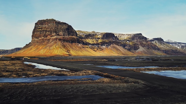Prise de vue par drone d'une montagne majestueuse en Islande, d'un bord de route spectaculaire et de champs enneigés. Collines massives islandaises et terres gelées brunes dans les paysages scandinaves. Ralenti.