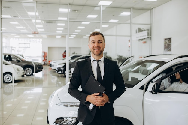 Une prise de vue rapprochée d'un assistant de magasin caucasien heureux, confiant et souriant tenant un bloc-notes dans des vêtements formels et regardant la caméra dans un magasin de concessionnaires d'automobiles.