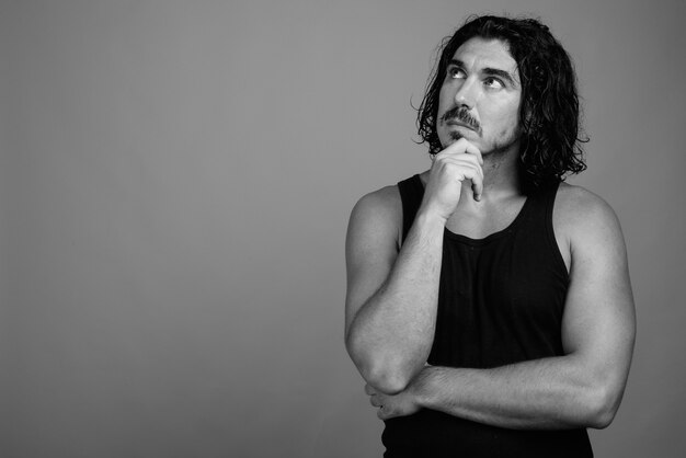 Prise de vue en studio d'un bel homme macho aux cheveux bouclés et à la moustache sur fond gris en noir et blanc