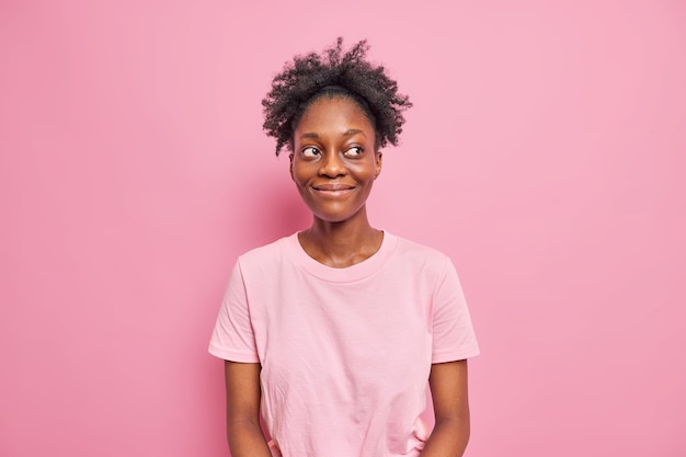 Prise de vue en studio d'une belle femme à la peau foncée qui détourne le regard avec une expression heureuse et satisfaite se sent bien a les cheveux bouclés