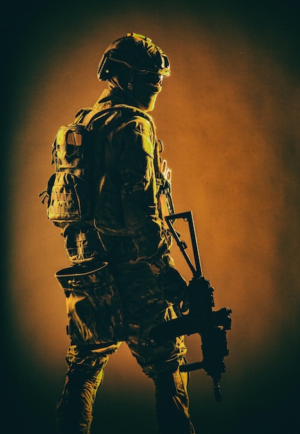 Prise de vue en studio discrète d'un soldat des forces spéciales de l'armée, d'un combattant commando en masque, de lunettes balistiques, d'un casque tactique et d'un uniforme de combat, tenant un fusil de service à canon court, regardant par-dessus l'épaule