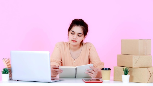 Prise de vue en studio d'une femme d'affaires asiatique heureuse et prospère, jeune entrepreneur en démarrage travaillant à table sur fond rose.