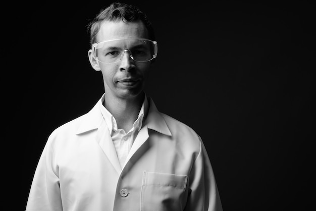 Prise de vue en studio d'un homme médecin portant des lunettes de protection contre un mur gris en noir et blanc