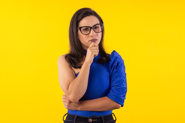 Prise de vue en studio d'une jeune femme à lunettes avec un chemisier bleu sur fond jaune avec une expression faciale