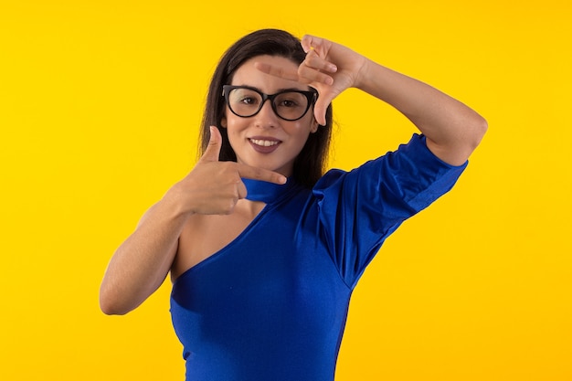 Prise de vue en studio d'une jeune femme à lunettes avec un chemisier bleu sur fond jaune avec une expression faciale