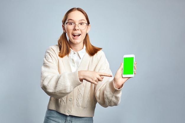 Prise de vue en studio d'une jeune fille souriante montre un écran vide de gadget et un téléphone intelligent porte un pull