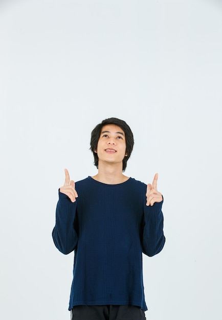 Prise de vue en studio d'un mannequin asiatique jeune beau adolescent mince en chemise à manches longues debout souriant tenant les mains pointant les doigts sur l'espace de copie vierge présentant le produit sur fond blanc