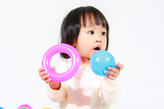 Prise de vue en studio d'un petit modèle asiatique de petite fille aux cheveux noirs courts et mignons en jupe à carreaux décontractée assis sur le sol souriant en riant jouant avec des balles rondes colorées jouet seul sur fond blanc.