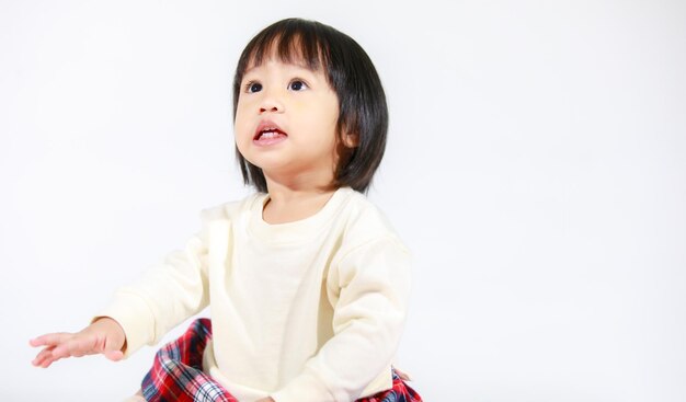 Prise de vue en studio d'un petit modèle mignon de petite fille asiatique aux cheveux noirs courts en jupe à carreaux décontractée assis et souriant sur fond blanc