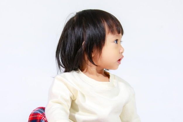 Prise de vue en studio d'un petit modèle mignon de petite fille asiatique aux cheveux noirs courts en jupe à carreaux décontractée assis et souriant sur fond blanc