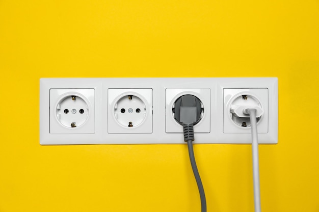 Prises de courant avec fiches insérées sur le mur jaune Alimentation électrique