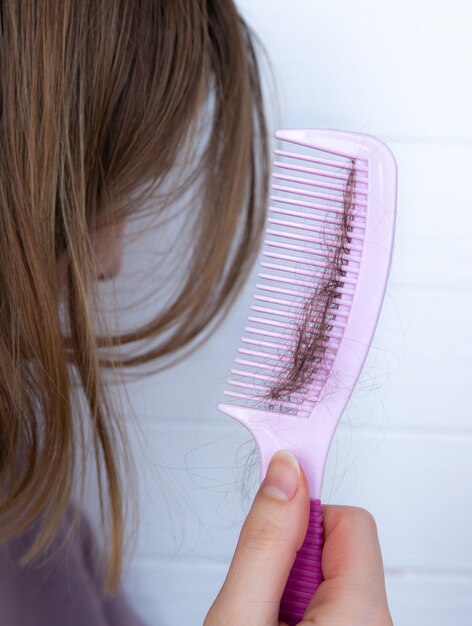 Problème de perte de cheveux. La femme tient avec un peigne rose.