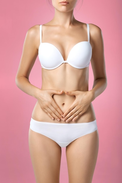 Photo problème de santé féminine closeup d'une femme avec un corps mince et en forme en culotte et soutien-gorge souffrant de douleur et tenant ses mains sur l'estomac troubles digestifs douleurs menstruelles problèmes de santé concept