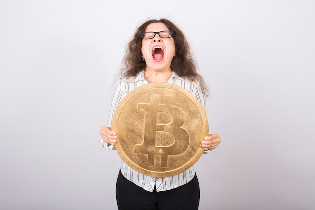 Problèmes d'économie - femme d'affaires choquée hurle et tenant le bitcoin d'or sur le mur blanc