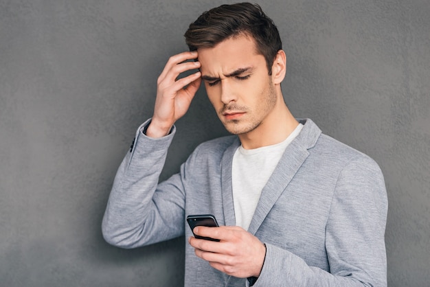 Problèmes quotidiens. Jeune homme pensif tenant un téléphone portable