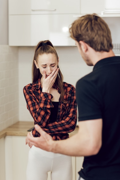 Problèmes de violence domestique et d'alcoolisme dans une jeune famille. Un homme ivre crie sur sa femme effrayée à la maison dans la cuisine et la menace de son poing. Une jeune femme effrayée qui pleure