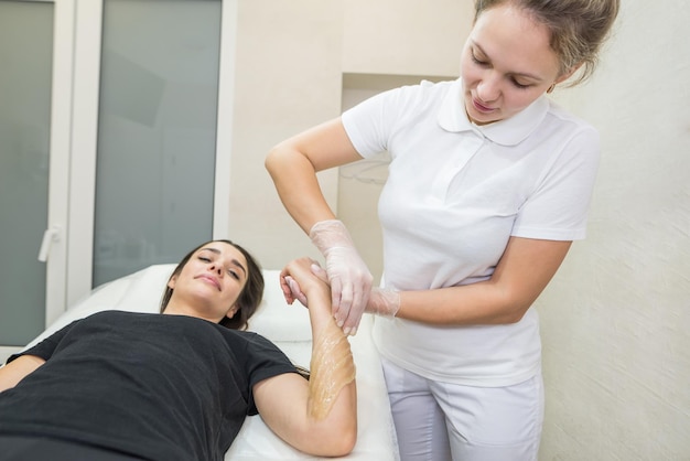 Procédure d'épilation à la pâte de sucre shugaring Le cosmétologue applique de la pâte de sucre à la main d'une jeune femmeÉpilation des mains féminines dans un salon de beauté