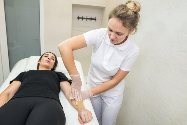 Procédure d'épilation à la pâte de sucre shugaring Le cosmétologue applique de la pâte de sucre à la main d'une jeune femmeÉpilation des mains féminines dans un salon de beauté