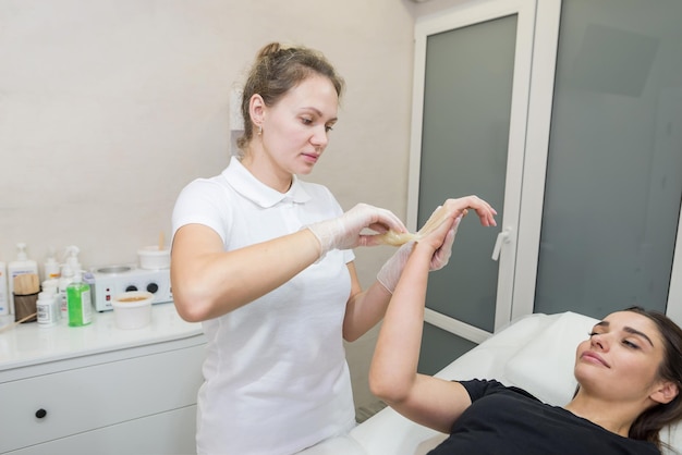 Procédure d'épilation à la pâte de sucre shugaring Le cosmétologue applique de la pâte de sucre à la main d'une jeune femme