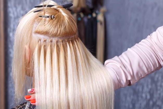 Procédure d'extensions de cheveux coiffeur fait des extensions de cheveux à la jeune fille blonde dans un salon de beauté se