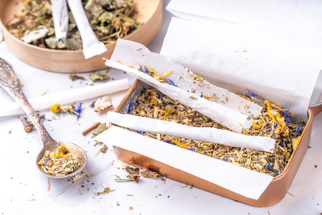 Procédure de préparation de cigarettes artisanales à la main avec un mélange d'herbes feuilles et fleurs avec des boîtes papier sur fond blanc