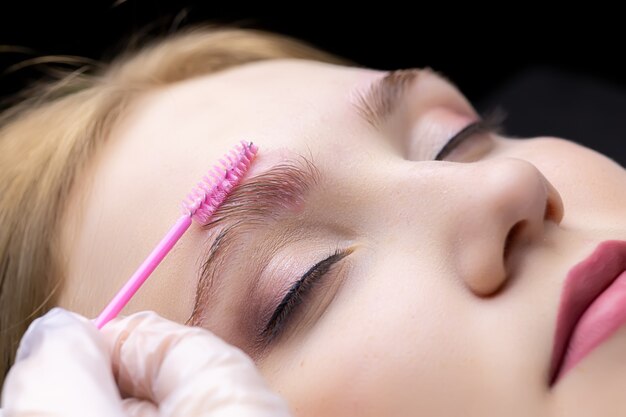 Procédure de stratification des sourcils le maître applique du gel avec un pinceau sur les sourcils du modèle