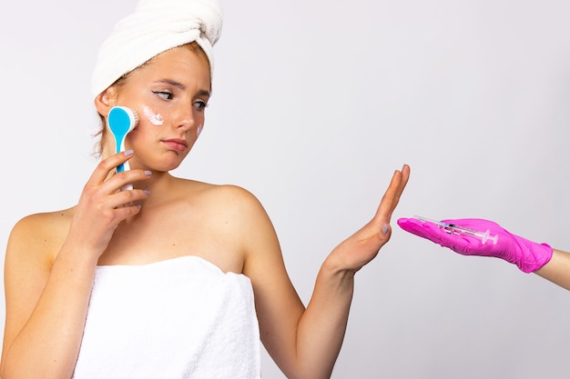 Procédures cosmétiques et soins de la peau du visage. La fille se fait un massage avec une brosse cosmétique, refusant les injections cosmétologiques. Mur blanc. Photo de haute qualité