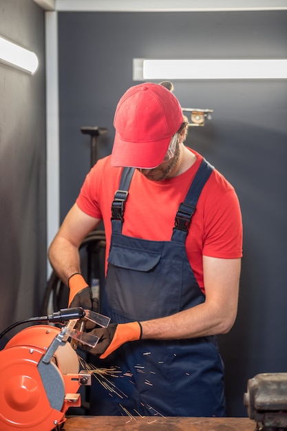 Processus D'affûtage. Homme En Bonnet Rouge Et Tshirt Impliqué Travaillant Sur L'affûteuse En Atelier