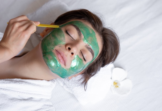 Le processus d'application d'un masque cosmétique vert sur le visage d'une jeune femme, la procédure de spa dans le salon, la beauté et les soins de la peau.