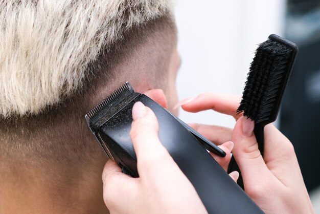 Processus de coupe de cheveux d'un jeune homme blond avec une tondeuse à cheveux dans un fauteuil dans un salon de coiffure, concept de salon de coiffure pour hommes et garçons